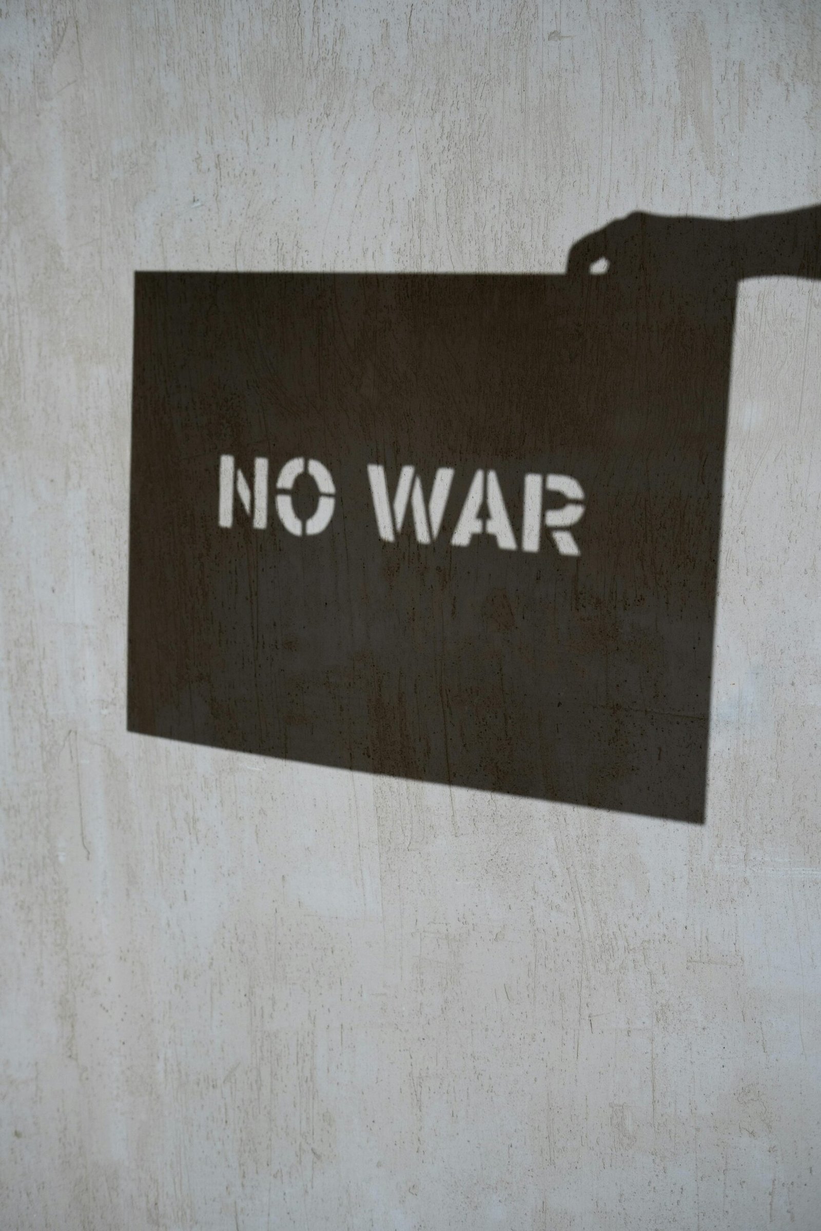 Shadow art depicting 'No War' message on a textured concrete wall, emphasizing peace.